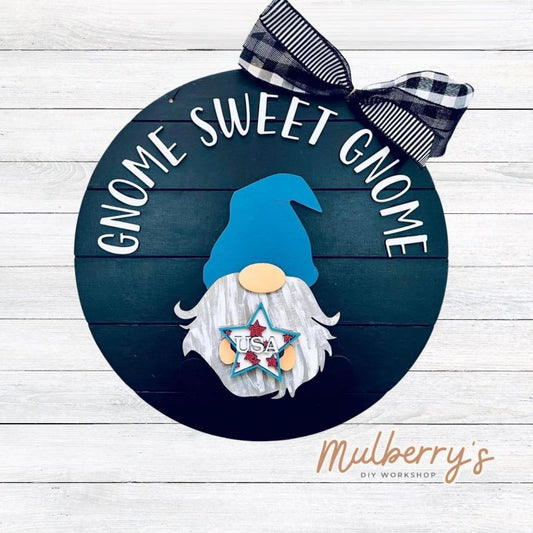 This sweet little fella will make you smile each season and holiday. Simply swap out his hands to create a brand new door hanger! The door hanger is approximately 18-inches in diameter and comes with or without greenery on the backer.  Includes Gnome Sweet Gnome door hanger with July 4th insert.