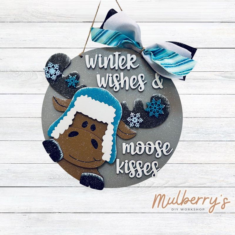 Our newest mini door hanger is moosetastic! Approximately 10.5" in diameter and includes your choice of a mini bow or beads.